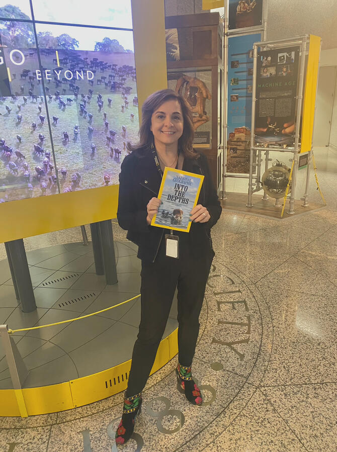 A woman standing at the middle of a room holding a copy of a National Geographic Magazine.