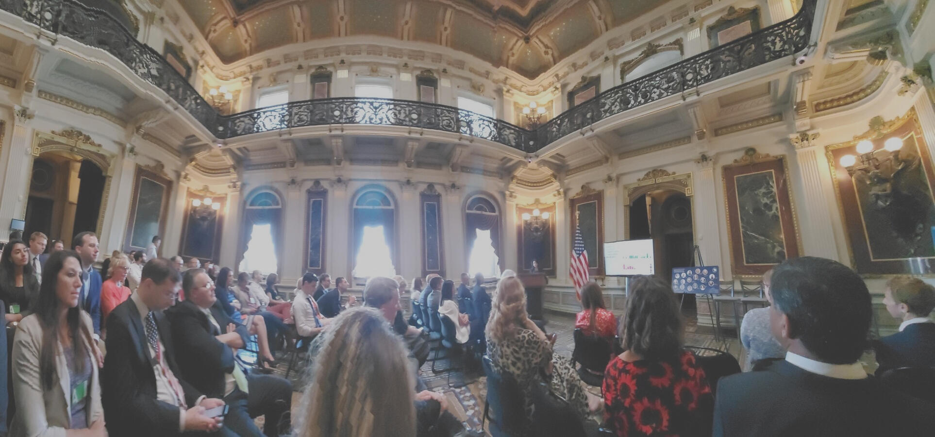 Audience members sitting in a large room. A woman (Davar Ardalan) is speaking at the podium