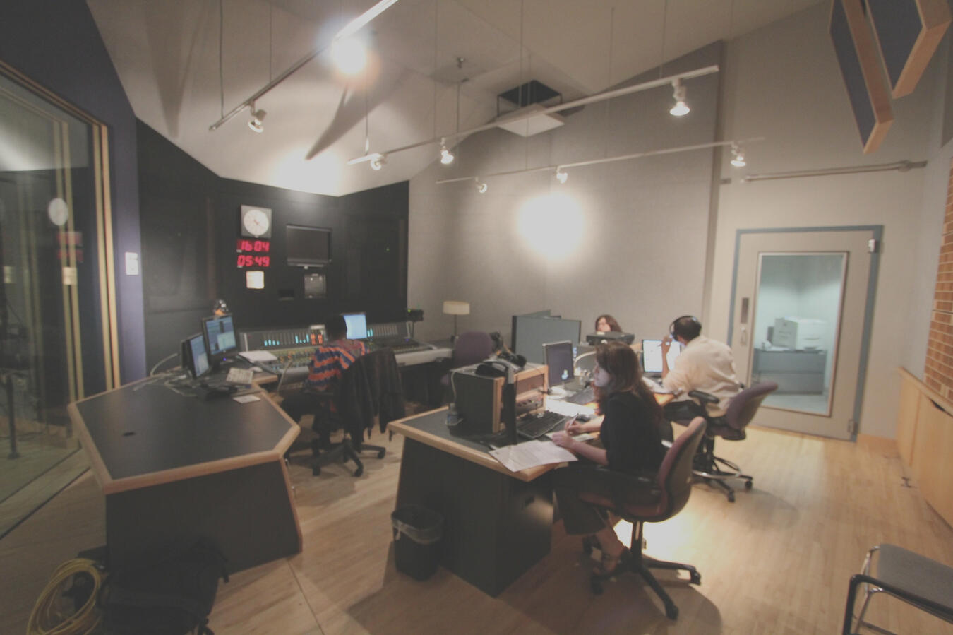 Image of a large studio with several people working including a woman at the forefront sitting on a chair and on a computer.